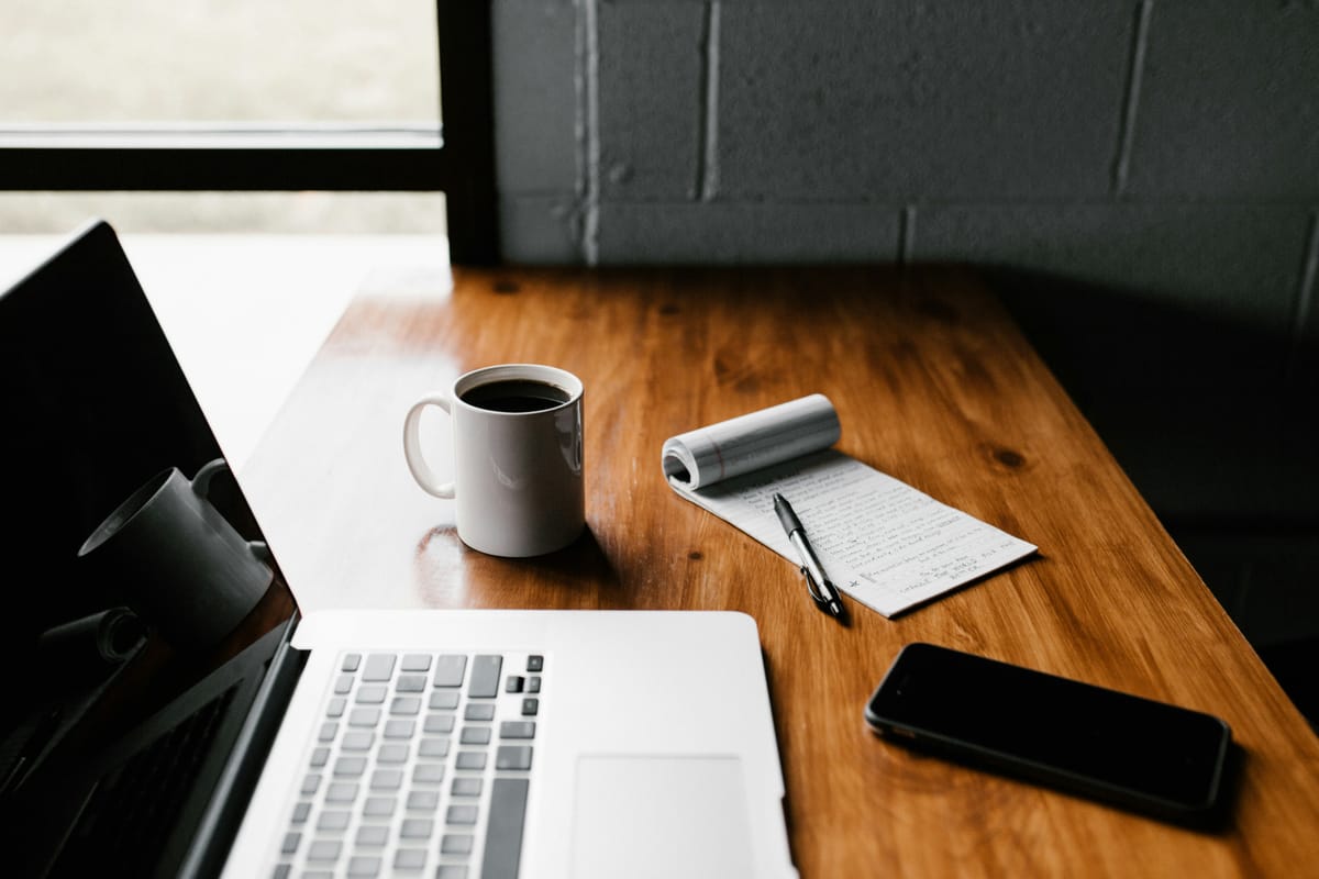 Laptop, smartphone, coffee, and notepad on a desk, reflecting a workspace for managing digital banking accounts